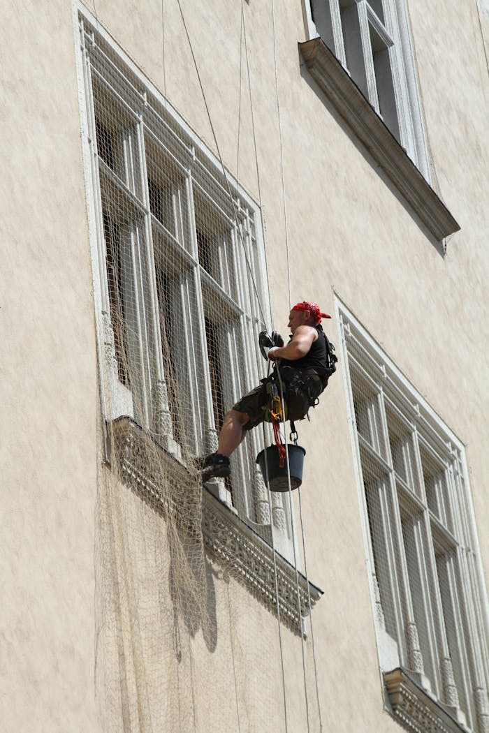 Worker cleaning high-rise windows with harness and safety gear.